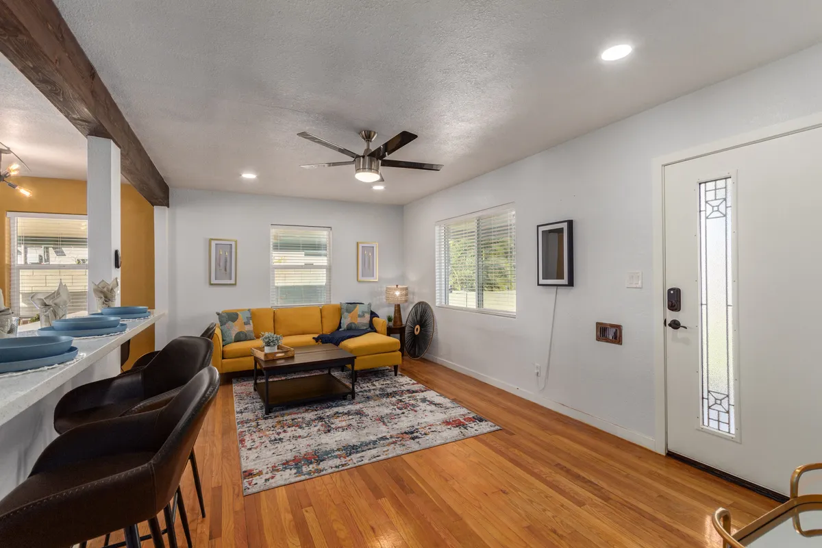 A cozy living lounge featuring a yellow sofa, stylish coffee table, soft rug, and curated artwork on the walls. An arched doorway is also visible, hinting at the home's historic architecture. The room is bright and welcoming, with ample daylight creating a comfortable atmosphere.