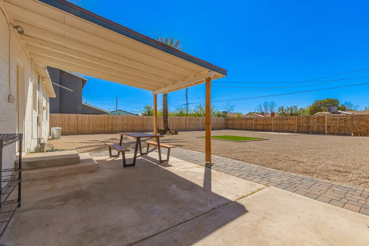 A spacious backyard featuring a covered patio with a picnic table, a sizeable grassy area, and secure fencing. The setting is relaxed and family-friendly, ideal for outdoor dining, games on the lawn, or playing with pets. The covered area offers shade for gatherings or meals al fresco, while the open lawn invites play and relaxation.
