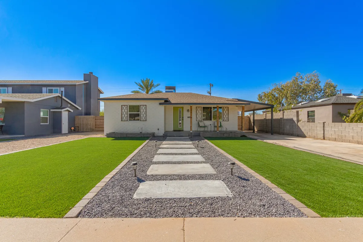 A warm, inviting exterior view of the home featuring a neatly maintained front lawn, a clear pathway leading to the house, and a charming facade. The sunlit scene feels peaceful and welcoming, with mature trees hinting at the established, leafy neighborhood setting.