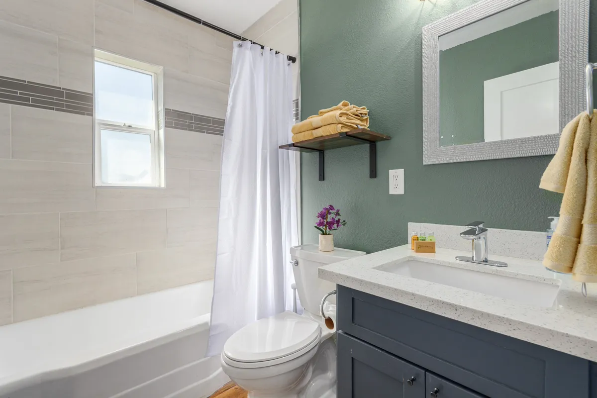 A modern yet inviting bathroom with a spacious bathtub, a stylish sink, neatly arranged towels, a mirror, and a shelf adorned with plants. The setting is both functional and relaxing, blending updated fixtures with a homey, spa-like feel.