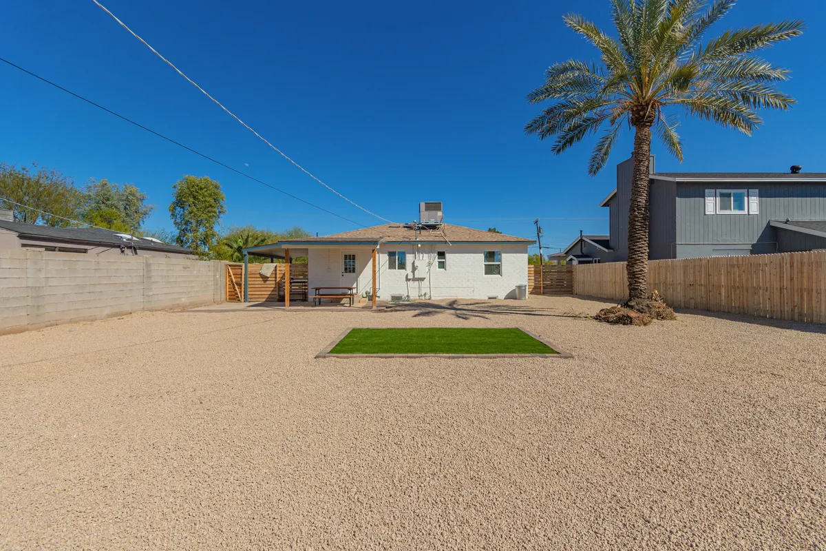 A welcoming view of the home’s exterior, featuring a lush grassy area shaded by a tall palm tree and the house’s inviting facade. The open green space is perfect for pets to stretch their legs or relax with their owners. The light and layout suggest a relaxed outdoor lifestyle ideal for pet-friendly stays.