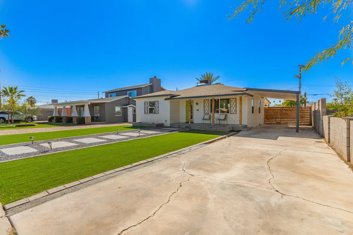 A wide-angle exterior view shows a green lawn, a front porch, and a paved driveway leading up to a home with modern architecture. The scene hints at neighborhood community events, family barbecues, and quiet evenings spent outdoors.